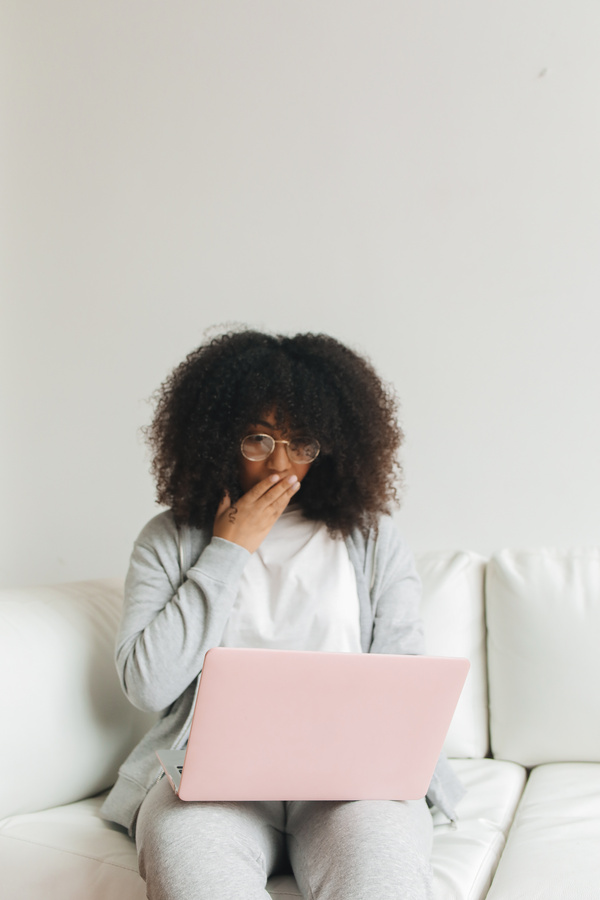 A Woman Using a Pink Laptop and Covering Her Mouth
